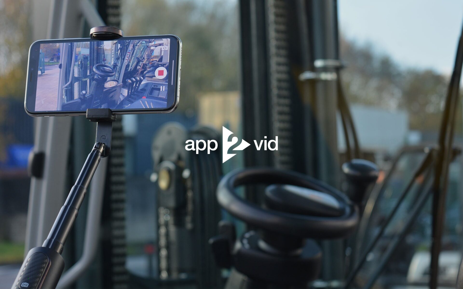 A smartphone on a tripod capturing video footage inside a vehicle cab, featuring the steering wheel and controls.
