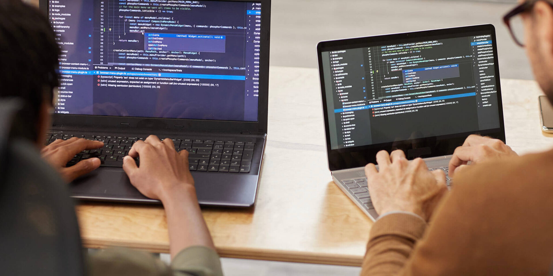 Two individuals coding on laptops with visible programming code on their screens