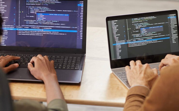Two individuals coding on laptops with visible programming code on their screens