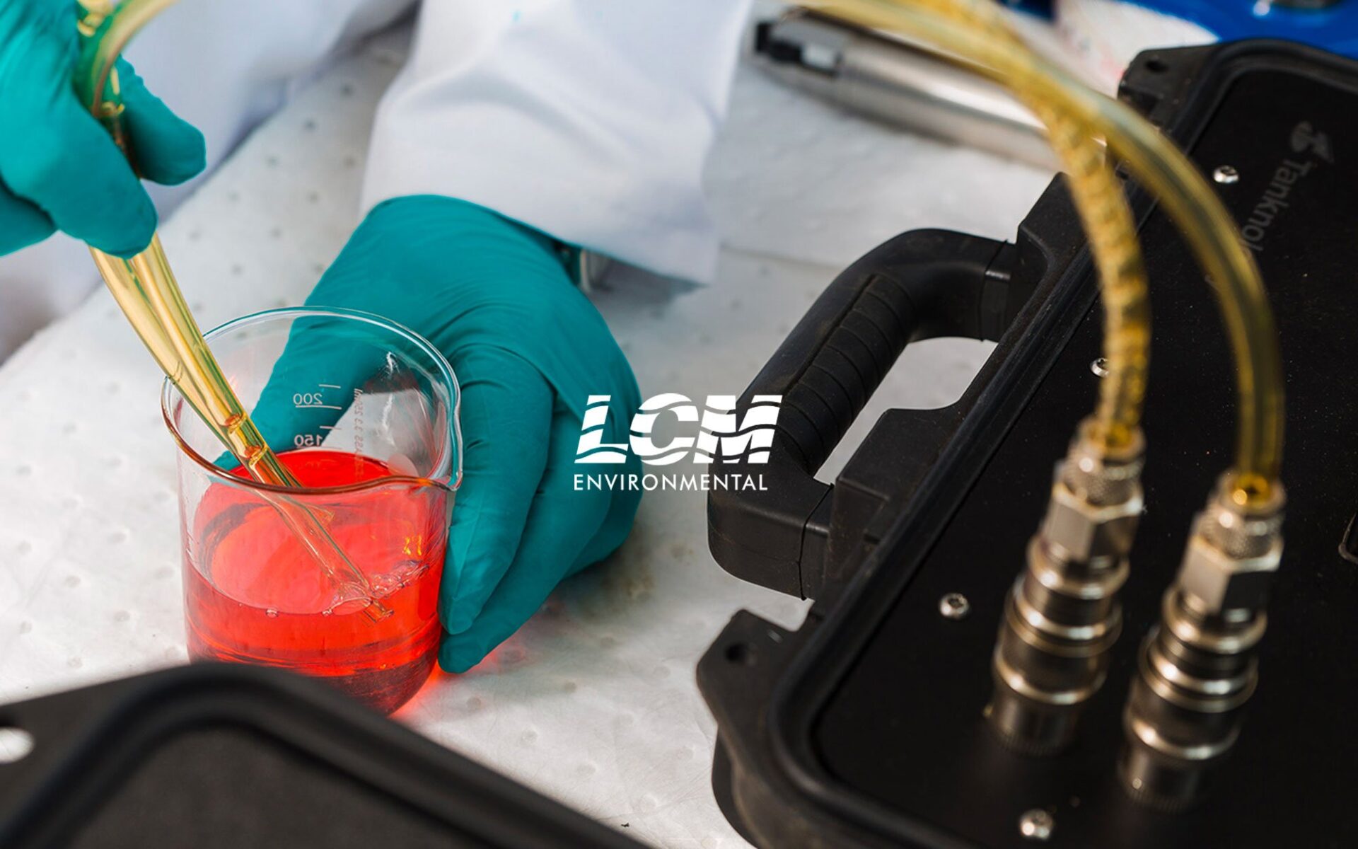 A scientist in a lab coat using pipettes to mix a bright red liquid in a glass beaker, with lab equipment visible in the background.