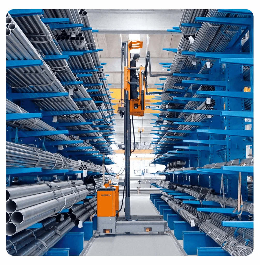 Vertical Storage System for Pipes and Metal Materials A vertical storage aisle with organized metal pipes and a lifting mechanism in a warehouse setting.