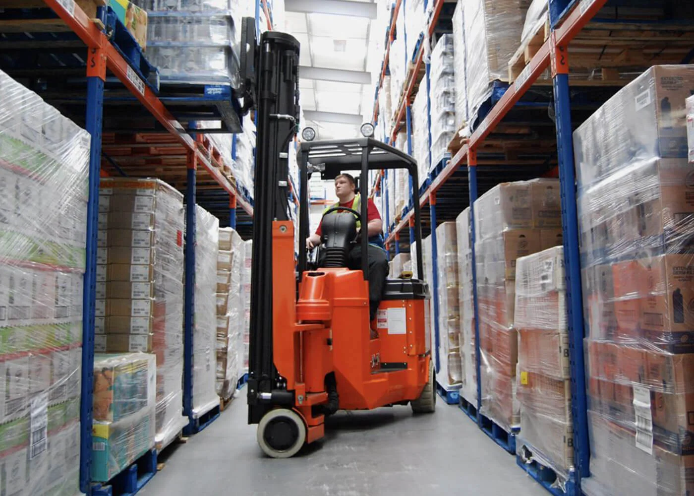 Warehouse Forklift in Action A forklift operator maneuvering through an aisle filled with stacked pallets in a warehouse.