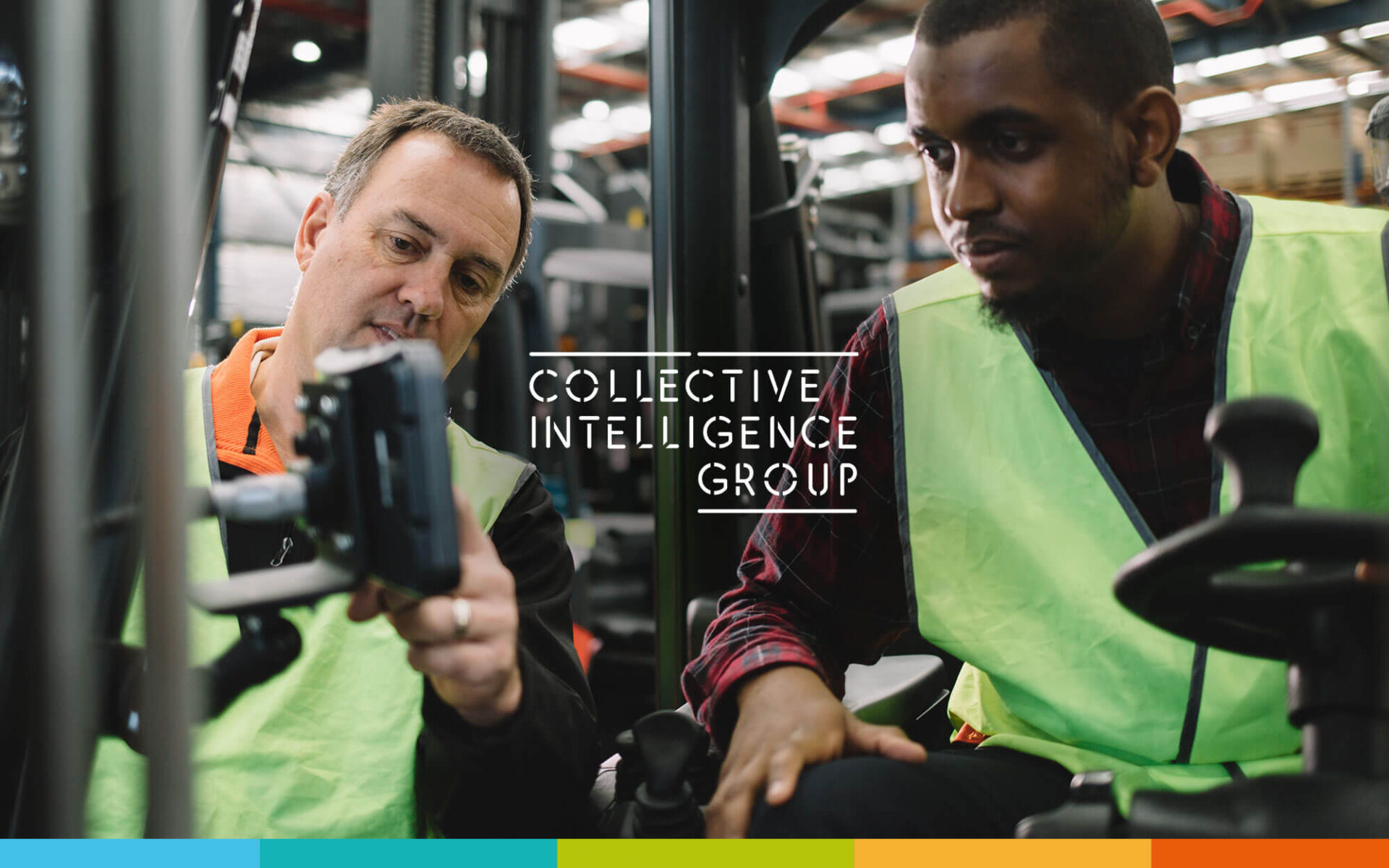 Two workers in vests examining a device in a warehouse setting, representing teamwork and collaboration at Collective Intelligence Group.