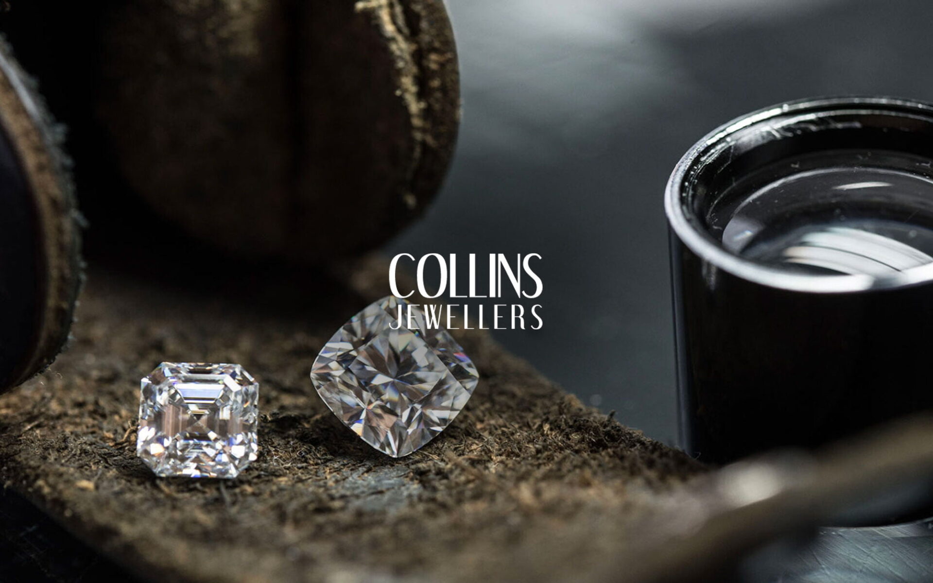 Two beautiful diamond gemstones resting on a leather surface with a jeweller's loupe nearby, featuring the logo of Collins Jewellers.