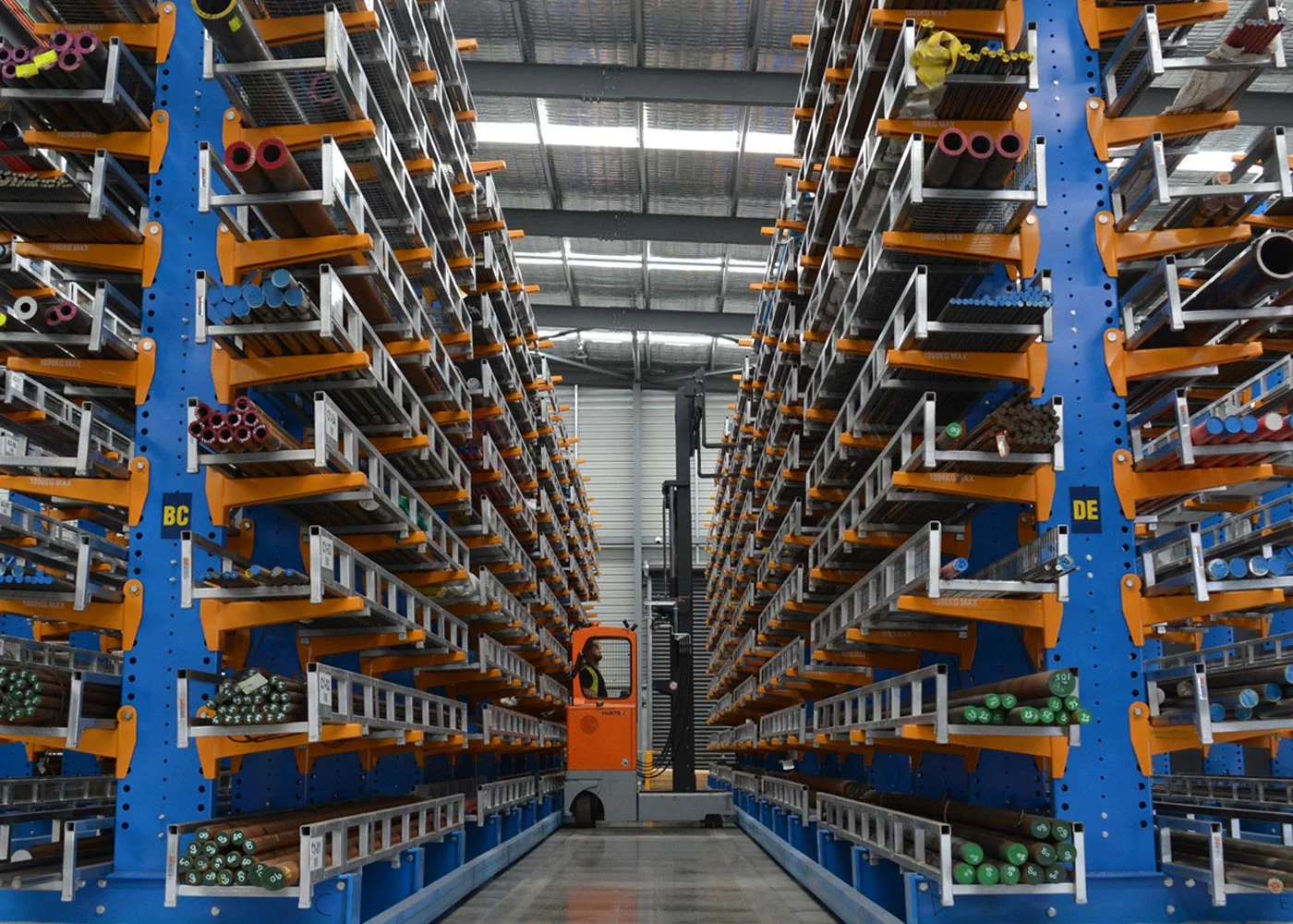 Efficient Warehouse Storage Racks with Forklift A view of a warehouse featuring multiple storage racks filled with pipes and a forklift in the aisle.