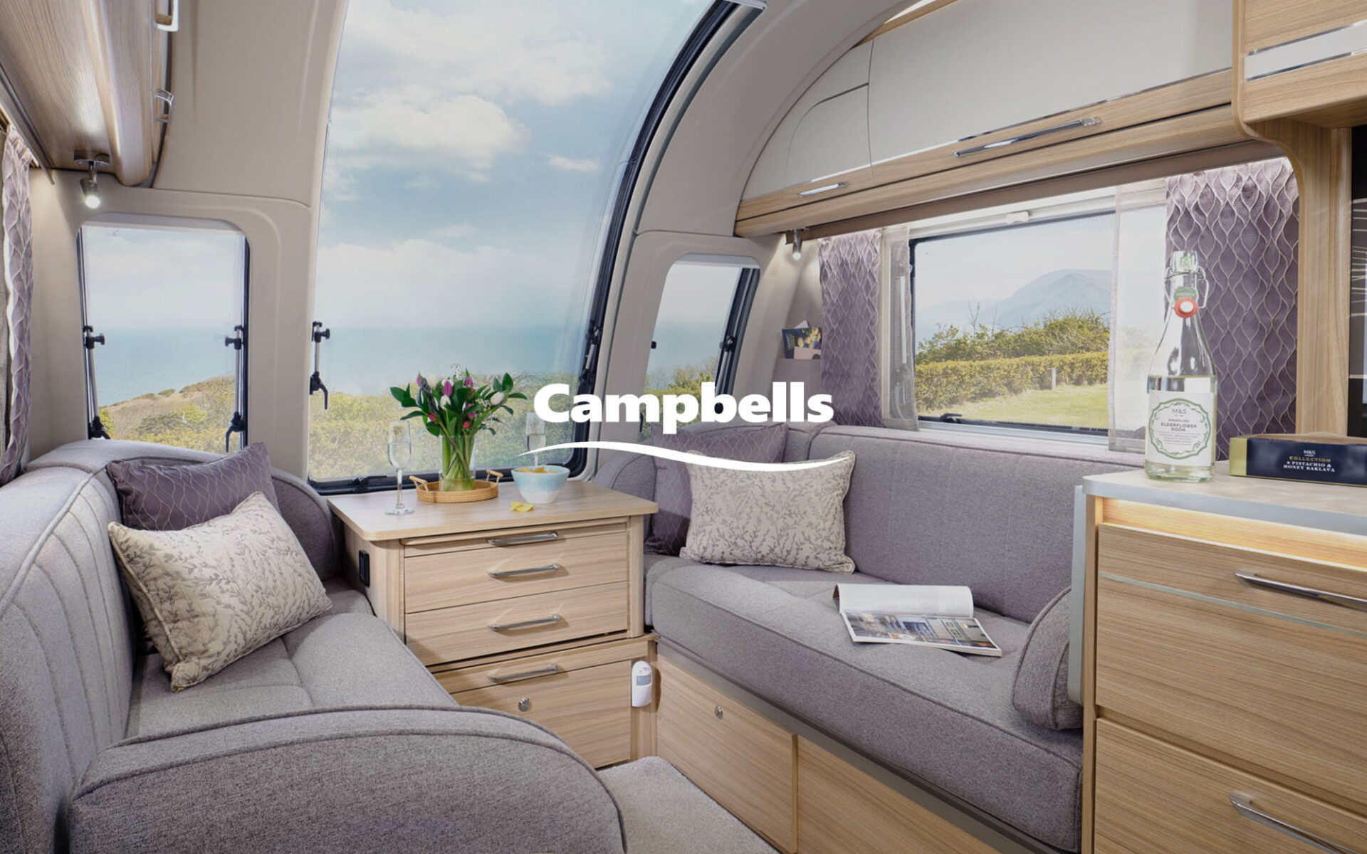Cozy interior of a caravan featuring a comfortable seating area, wooden cabinetry, and a scenic window view.
