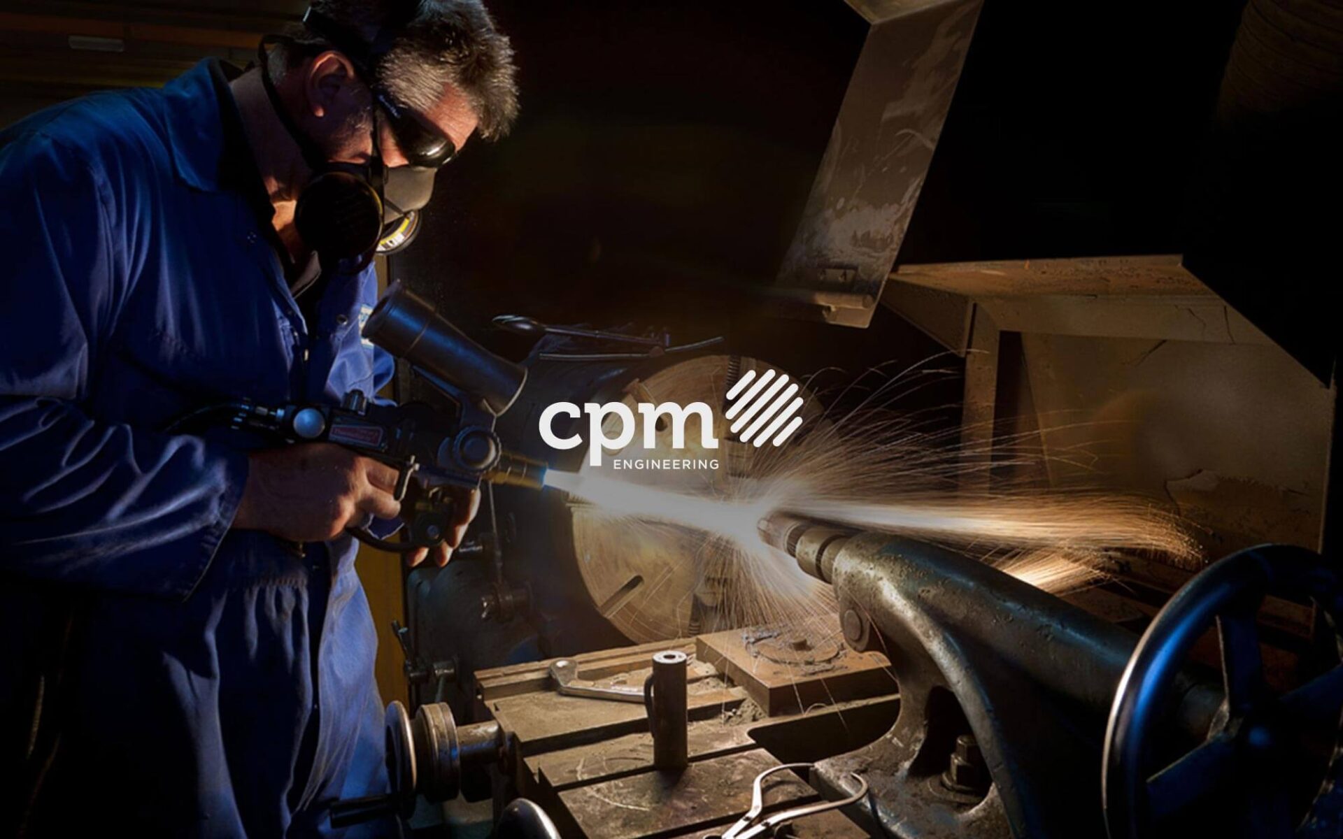 A skilled technician wearing a mask operates a spray gun in a machining workshop, with sparks flying from the workpiece.