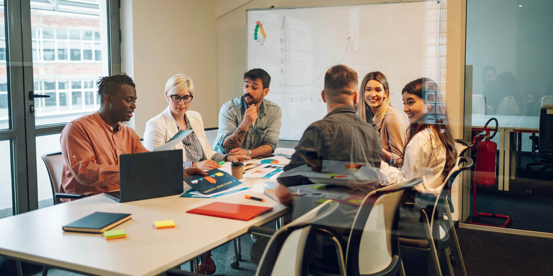 A diverse group of professionals collaborating around a conference table with laptops and notes in a bright modern office.