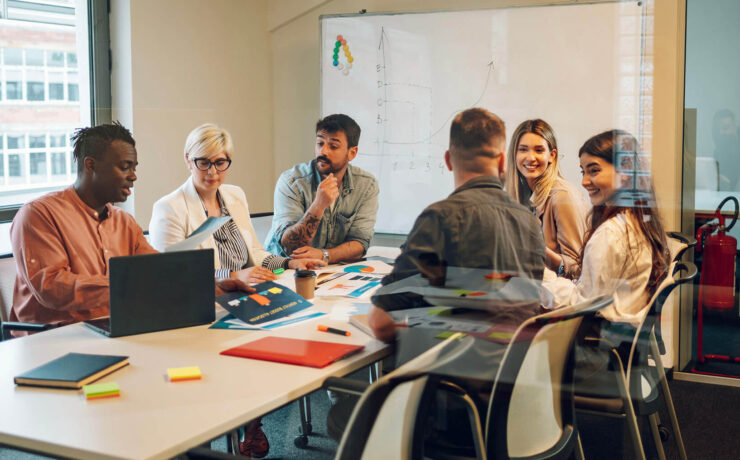 A diverse group of professionals collaborating around a conference table with laptops and notes in a bright modern office.
