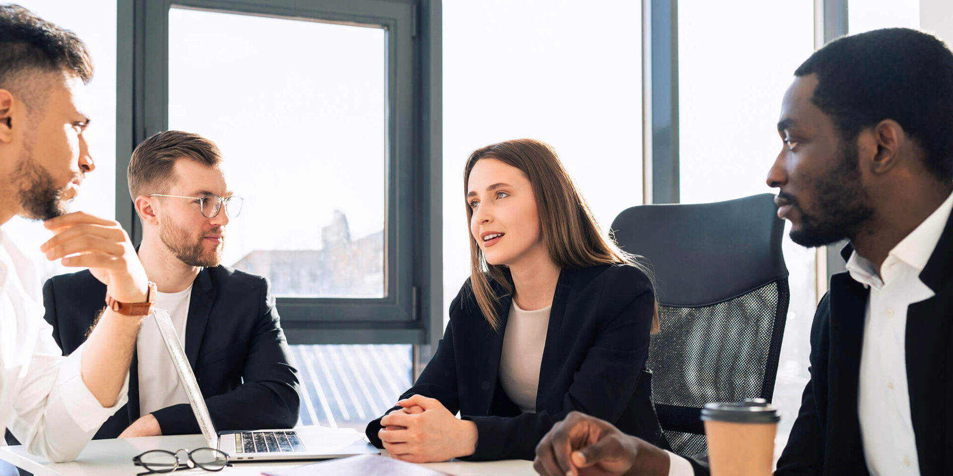 A diverse group of professionals engaged in a discussion around a conference table in a modern office.