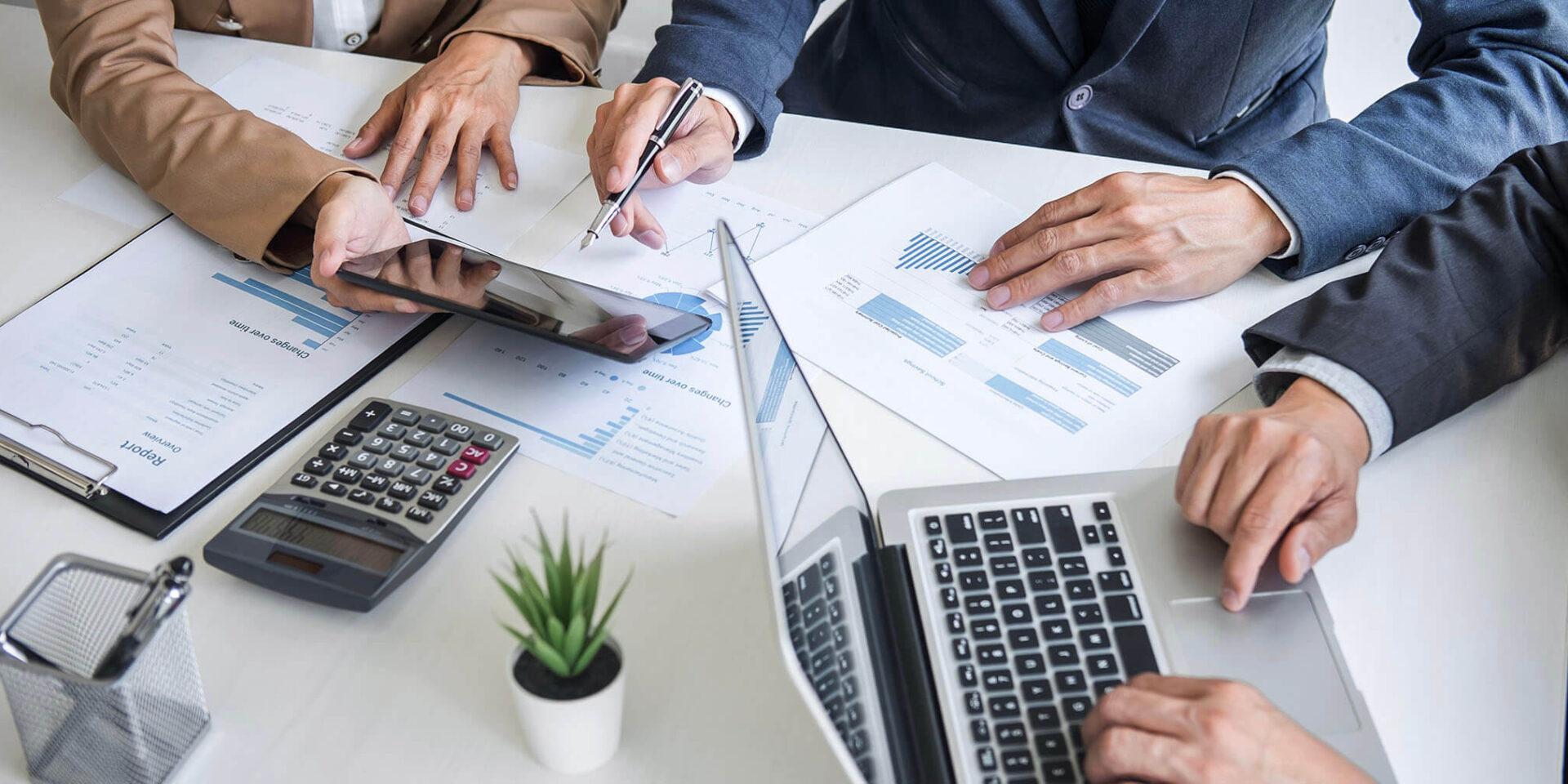 Close-up of hands engaged in a business meeting with laptops, financial documents, and a calculator on the table