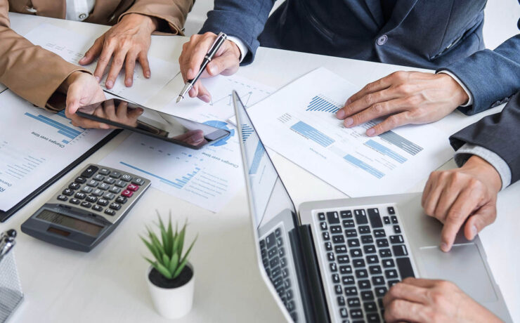 Close-up of hands engaged in a business meeting with laptops, financial documents, and a calculator on the table