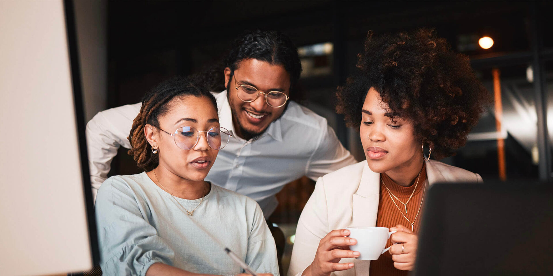 A diverse team collaborating on a project in a contemporary office setting, with one member reviewing work and others engaging in discussion.
