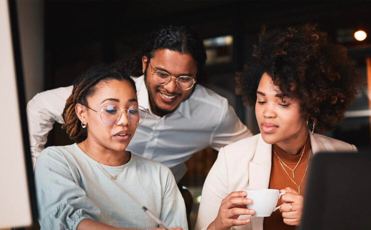 A diverse team collaborating on a project in a contemporary office setting, with one member reviewing work and others engaging in discussion.